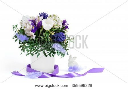 Easter Composition. Spring Flowers With Feathers, Purple Ribbon And Easter Bunny On A White Backgrou