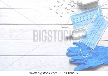 Medical Protective Mask, Rubber Gloves, Antiseptic And White Anti-irus Tablets Lie On A White Wooden
