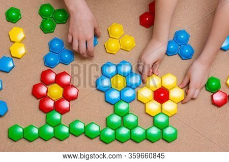 Children’s Hands Put The Details Of Colored Mosaics Into A Drawing Of Flowers On The Table. Leisure 
