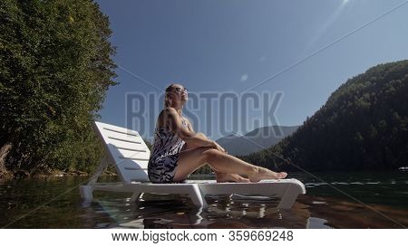 Woman Lie On A Sunbed In Sunglasses And A Boho Silk Shawl. Girl Rest On A Flood Wood Underwater Pier
