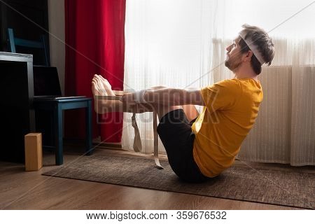 Young Man Practices Yoga In Navasana Asana Using Belt. Male Yogi In Boat Pose