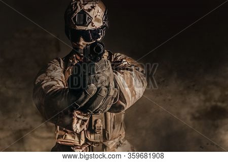 Photo of a fully equipped soldier in armor, helmet, gloves and glasses gun aiming pose on dustry desert background.