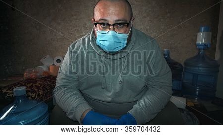 Man In Protective Mask Sits Home With Food Supplies And Watches Tv News About Coronavirus Covid-19b,