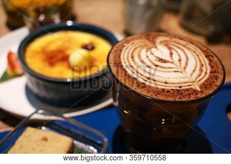 Cafe Latte With Latte Art On A Cup With Vanilla Crème Brûlée On The Background.