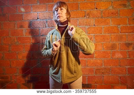 A Middle-aged Woman Poses Showing Clothes Near Red Brick Wall. An Inept Model In An Inept Shoot