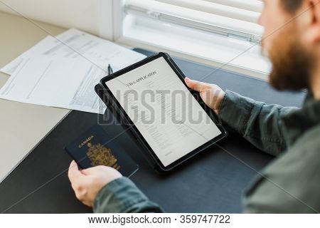 Male Person Reading Visa Application On Tablet And Holging Passport.
