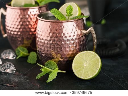 Moscow Mule Cocktail In A Copper Mug With Lime And Mint And Wooden Squeezer On Dark Kitchen Backgrou