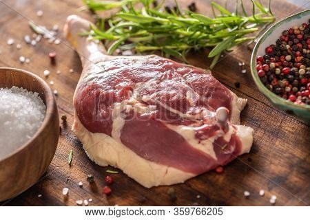 Close-up View Of A Raw Unskinned Duck Leg With Pepper, Rosemary And Salt On A Dark Wooden Background