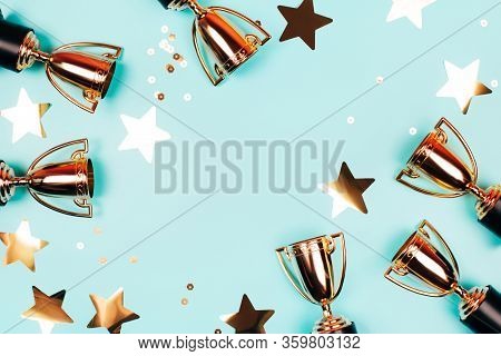Golden Cups Of Winner With Shiny Confetti On A Blue Background With Copy Space. Flat Lay Style.