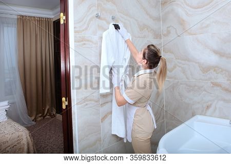 The Maid In The Bathroom Hangs A White Terry-cloth Robe On A Hanger. The Concept Of The Hotel Busine
