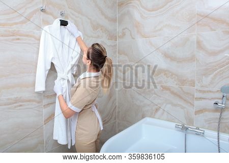 The Maid In The Bathroom Hangs A White Terry-cloth Robe. The Concept Of Service To Our Guests. Copy 