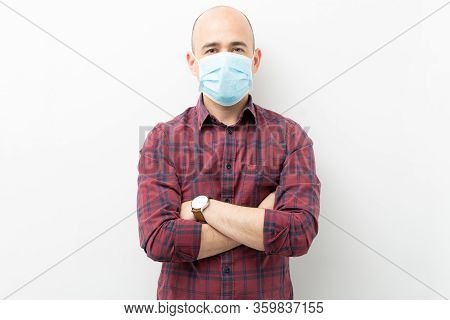 Caucasian Man In His 30s Wearing A Surgial Mask With His Arms Crossed And Looking Serious During Cov