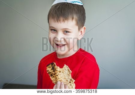 Cute Caucasian Child In A White Kippah Cap Eating Shmura Matzo, A Piece Of Traditional Jewish Unleav