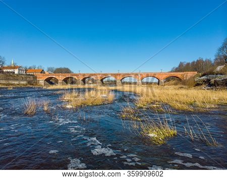 Beautiful Sunny View Of River Wenta Flowing Towards Old Brick Bridge In Old Historic Countryside Cit