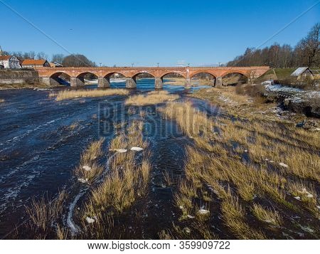 Beautiful Sunny View Of River Wenta Flowing Towards Old Brick Bridge In Old Historic Countryside Cit