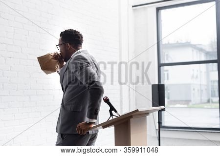 Nervous African American Speaker Breathing With Paper Bag And Having Panic Attack During Business Co