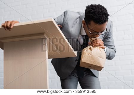 Nervous African American Businessman Breathing With Paper Bag And Having Panic Attack During Busines