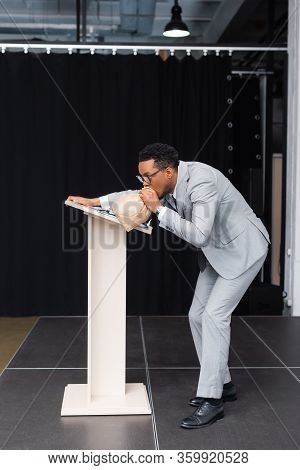 Stressed African American Speaker Breathing With Paper Bag And Having Panic Attack On Business Confe