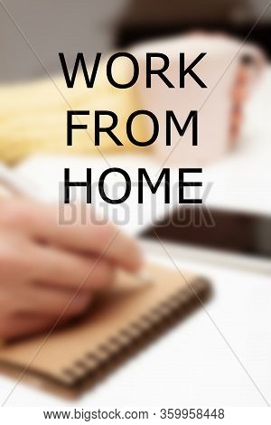 The Inscription Work At Home, Against The Background Of A Hand Writing In A Notebook Holding A Cup O