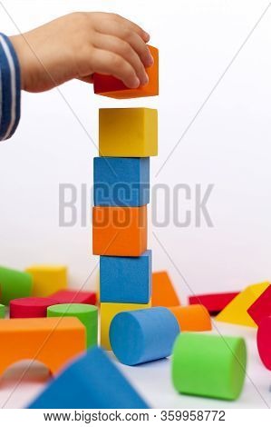 A Child Builds A Pyramid Of Cubes On A White Background. The Boy's Hand Holds A Cube.