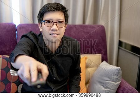 Asian Happy Man Using Remote Controller While Watching Tv Sitting On Sofa In Living Room. Domestic L