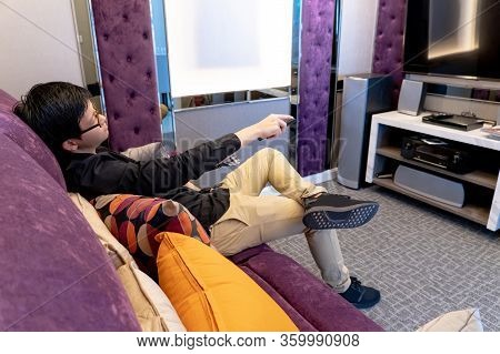 Asian Happy Man Using Remote Controller While Watching Tv Sitting On Sofa In Living Room. Domestic L