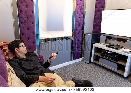 Asian Happy Man Using Remote Controller While Watching Tv Sitting On Sofa In Living Room. Domestic L