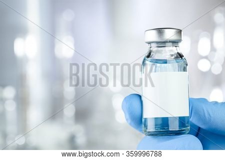Healthcare concept with a hand in blue medical gloves holding a vaccine vial with blue liquid and black white label
