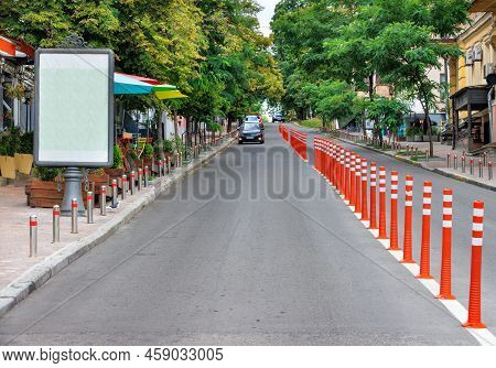 The Straight Line Of The Carriageway Of The Road Surface Is Divided By Orange Columns Against The Ba