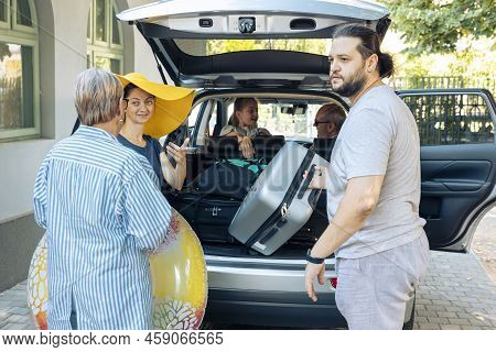 European Family Loading Baggage In Trunk Of Car To Leave On Seaside Vacation With Small Kid, Parents