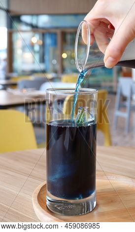 Woman's Hand Pouring Butterfly Pea Flower Tea Onto An Ice Cube In A Glass