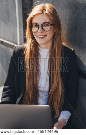 Caucasian Businesswoman Working With Her Laptop Sitting On A Park Bench In The Urban City, Looking A