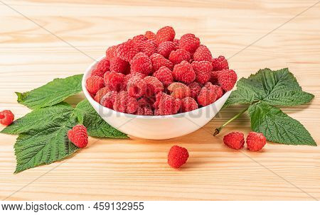Raspberries On White Plate On Wooden Table With Leaves. Organic Raspberries Grown Without Use Of Che