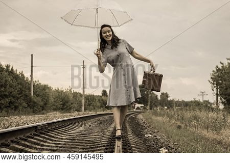 A Happy Smiling Young Woman With An Umbrella And A Brown Vintage Suitcase Walks Merrily Along The Ra