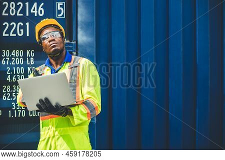Black African Worker Working In Logistic Shipping Using Laptop To Control Loading Containers At Port