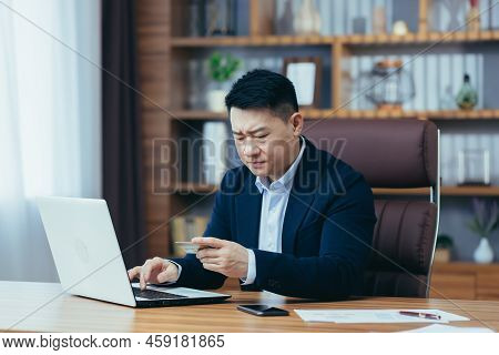 Upset Asian Man, Trying To Make An Online Purchase, Sitting In The Office, Uses A Credit Card, And A