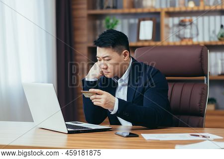 Upset Asian Man, Trying To Make An Online Purchase, Sitting In The Office, Uses A Credit Card, And A