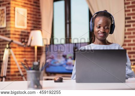 Young African American Woman In Headphones Watching Videos On Laptop At Home. Smiling Female Student