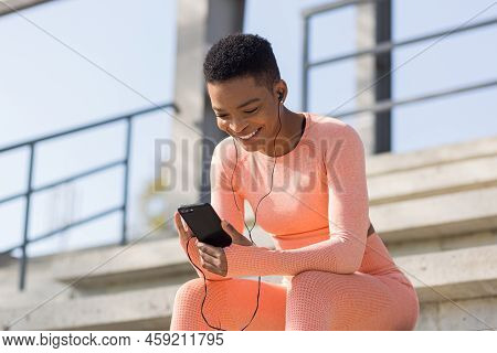 Beautiful And Successful Female Athlete Smiling Listens To Audio Book From Mobile Phone During Morni