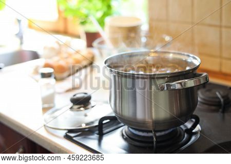 Shiny Pot With Boiling Water On Stove Indoors. Space For Text