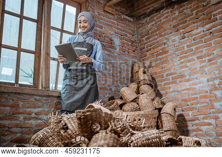 Craftswoman In Veil Standing Holding Tablet Among Woven Water Hyacinth