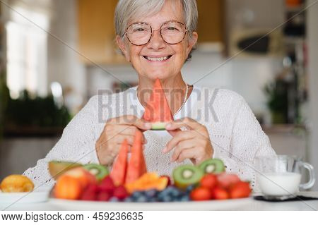 Beautiful Happy Senior Woman Holding A Slice Of Watermelon While Having Breakfast At Home With Fresh