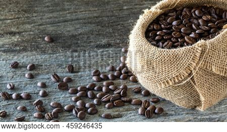 A Burlap Sack Filled With Coffee Beans And Many Spilled Out In Front.