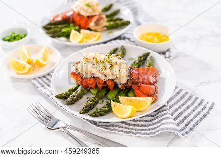 Sering Garlic Lobster Tails With Steamed Asparagus And Lemon Wedges On A White Plate.