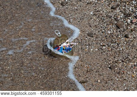 Wave Throws A Tin Can Filled With Plastic Floating In The Sea Onto Shore. Concept - Environmental Po