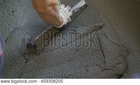 Leveling The Building Mix On The Floor With A Spatula. A Worker Spreads The Cement Mixture Over The 