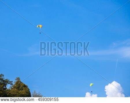 Two Paragliders With A Multicolor Wings Gliding In The Air In Front Of A Blue Sky During A Sunny Aft