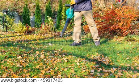 Lawn Care With A Blower. Removing Fallen Leaves With A Blower. The Gardener Holds A Blower In His Ha