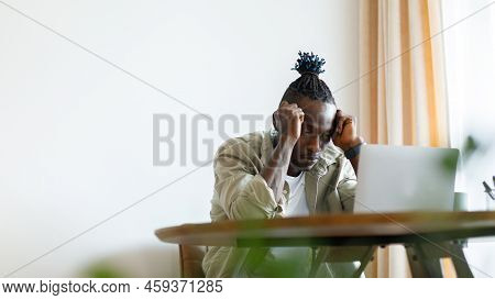 A Man Sits At Home In A Tense Mood And Looks At A Laptop. The Man Looks Flustered, With Hands Touchi