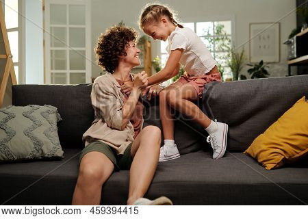 Cute Cheerful Girl And Her Happy Mother Laughing While Relaxing On Couch
